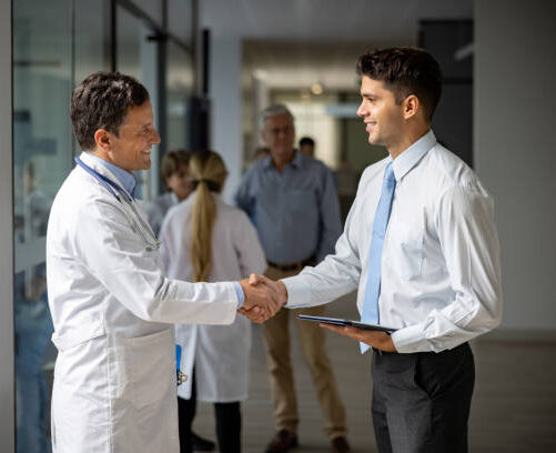 Latin American medical sales representative greeting a doctor with a handshake at the hospital while presenting some medicines - pharmaceutical industry concepts